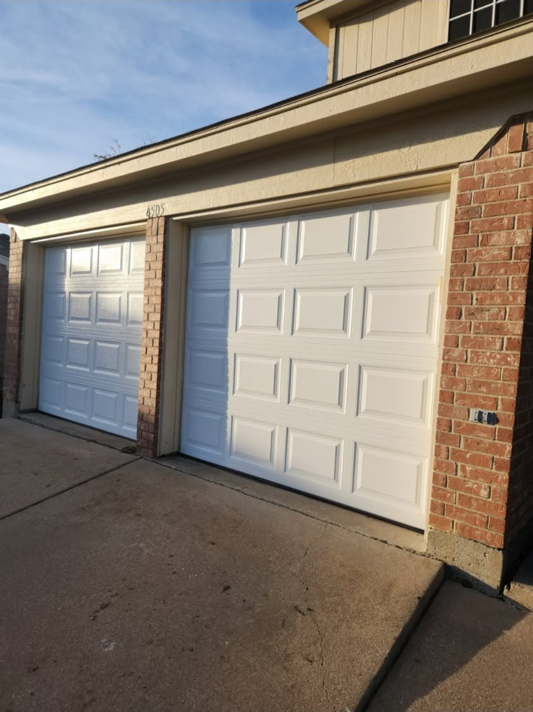 Two white short-panel garage doors installed on a brick home